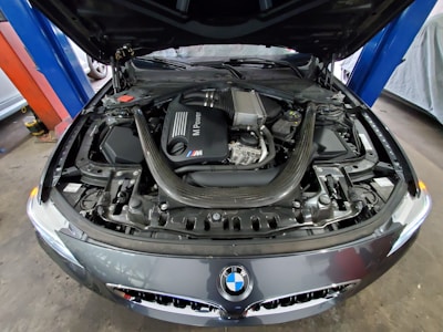 BMW car hood open with diagnostic equipment attached, showing battery check.