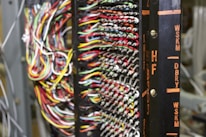 A detailed network or electronic panel features a complex array of multicolored wires organized in rows, connected to a central frame with labeled indicators. The labels on the frame, such as HF and DBRY, suggest its use in telecommunications or electronics. The arrangement of wires indicates intricate circuitry or data connection points.