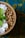 A wooden bowl filled with granola, coconut flakes, and a fresh mint leaf. The background features a textured surface in shades of blue and yellow.