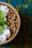 A wooden bowl filled with granola, coconut flakes, and a fresh mint leaf. The background features a textured surface in shades of blue and yellow.