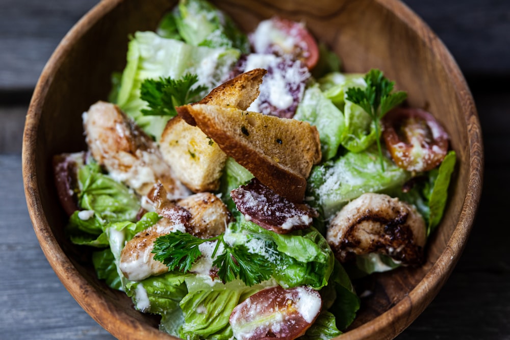 a wooden bowl filled with lettuce and meat