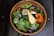 A close-up of a handcrafted wooden salad bowl filled with fresh greens and colorful vegetables.