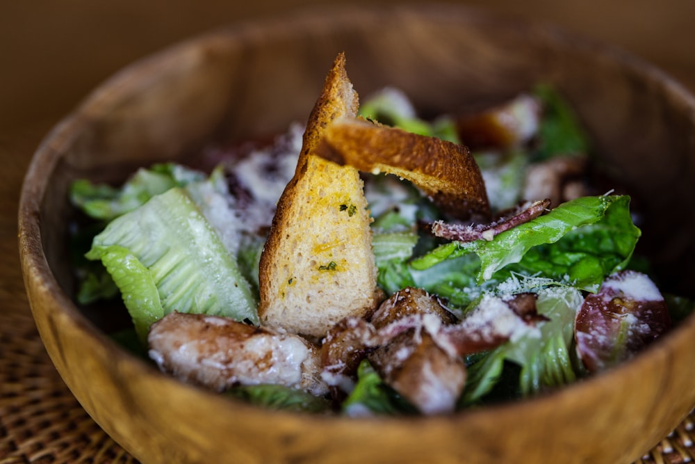 a wooden bowl filled with a salad topped with croutons