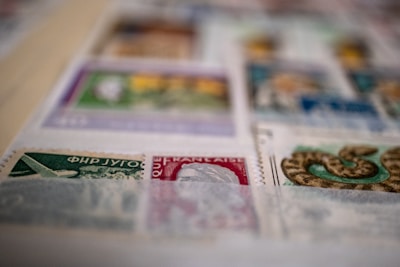A close-up view of a collection of postage stamps displayed on a page. The stamps vary in color and design, featuring illustrations such as an airplane and a snake. The image is slightly out of focus in some areas.