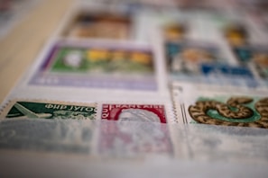 A close-up view of a collection of postage stamps displayed on a page. The stamps vary in color and design, featuring illustrations such as an airplane and a snake. The image is slightly out of focus in some areas.