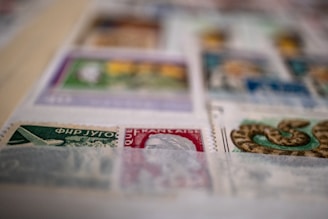 A close-up view of a collection of postage stamps displayed on a page. The stamps vary in color and design, featuring illustrations such as an airplane and a snake. The image is slightly out of focus in some areas.