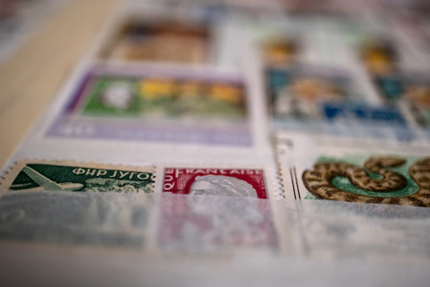 A close-up of a hand holding a vintage USPS stamp with a blurred mailbox in the background.