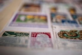 A close-up view of a collection of postage stamps displayed on a page. The stamps vary in color and design, featuring illustrations such as an airplane and a snake. The image is slightly out of focus in some areas.