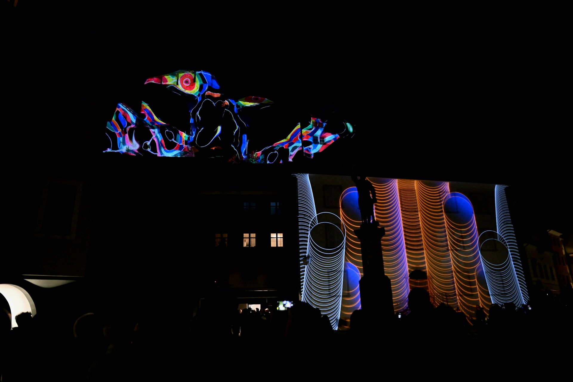 A mesmerizing architectural projection mapping display illuminating the façade of a historic building in Mérida with vibrant magenta and cyan patterns.