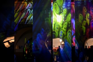 A series of overlapping digital projections create a vibrant collage of swirling patterns in green, blue, pink, and yellow. These abstract patterns are superimposed over an architectural scene with arched doorways and silhouettes of people. The colorful lights give the setting an otherworldly appearance.