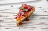 A creamy cheesecake garnished with a drizzle of raspberry sauce and mint leaves.