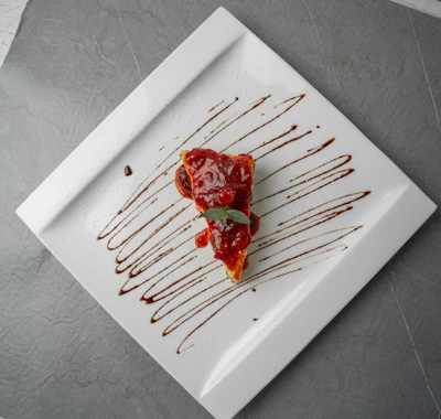 A slice of moist velvet cake topped with fresh berries and a drizzle of chocolate sauce on a white plate