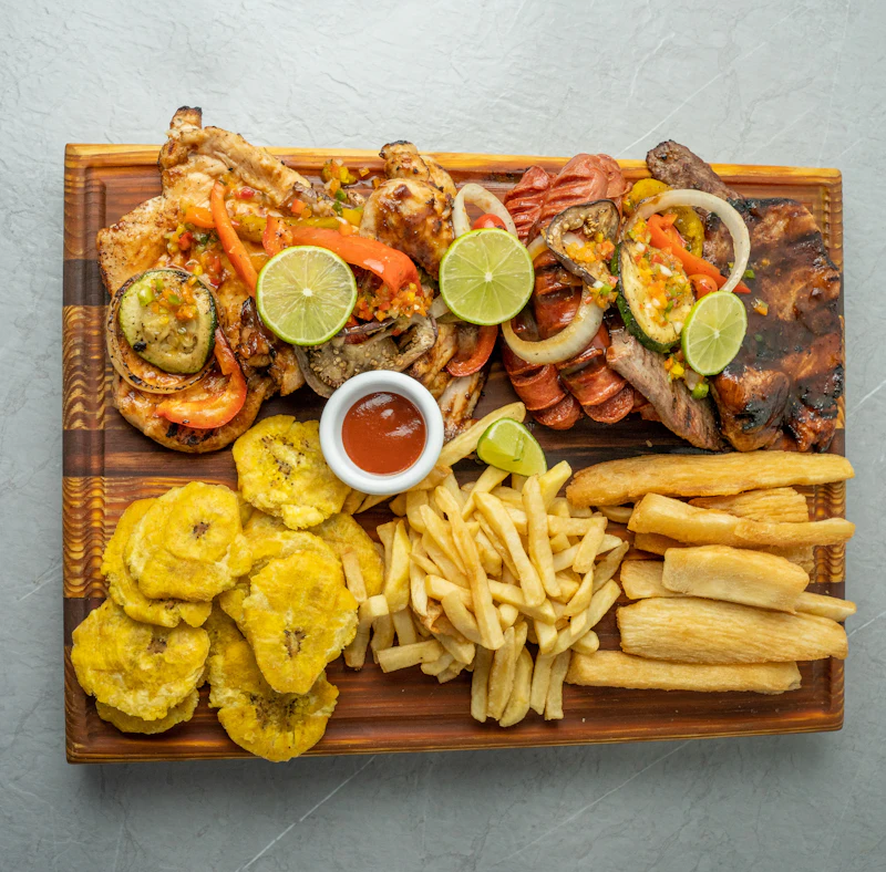 Picada con carnes, patacón, yuca y papas fritas sobre tabla de madera