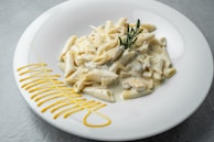 A chef’s hands garnishing a plate of penne with grated parmesan and parsley.