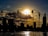 A construction worker confidently standing on a sturdy scaffold at a large industrial site during sunset.