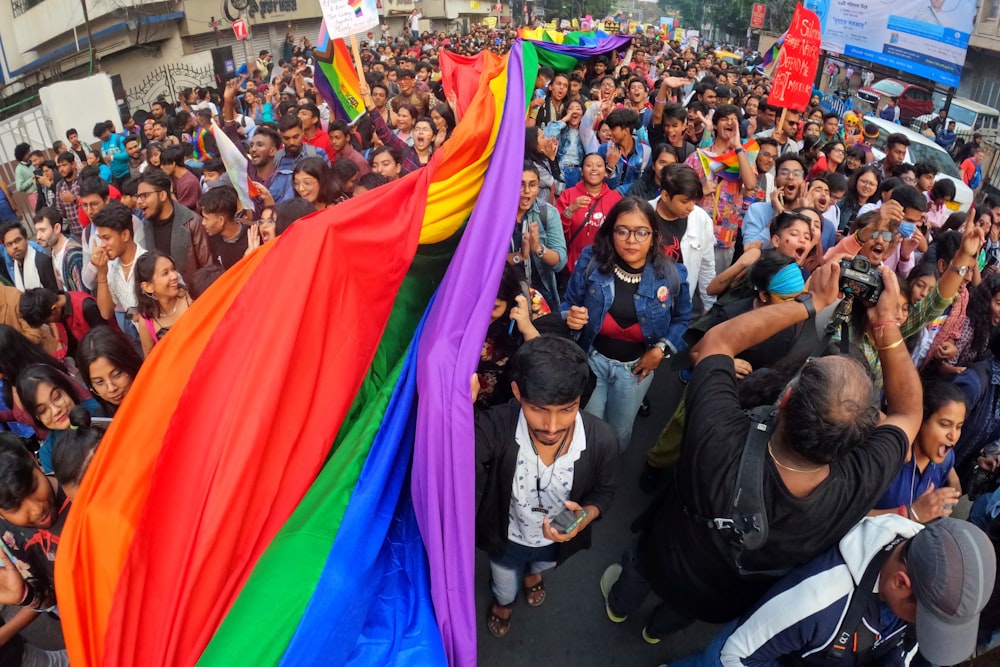 a crowd of people walking down a street holding a rainbow flag
