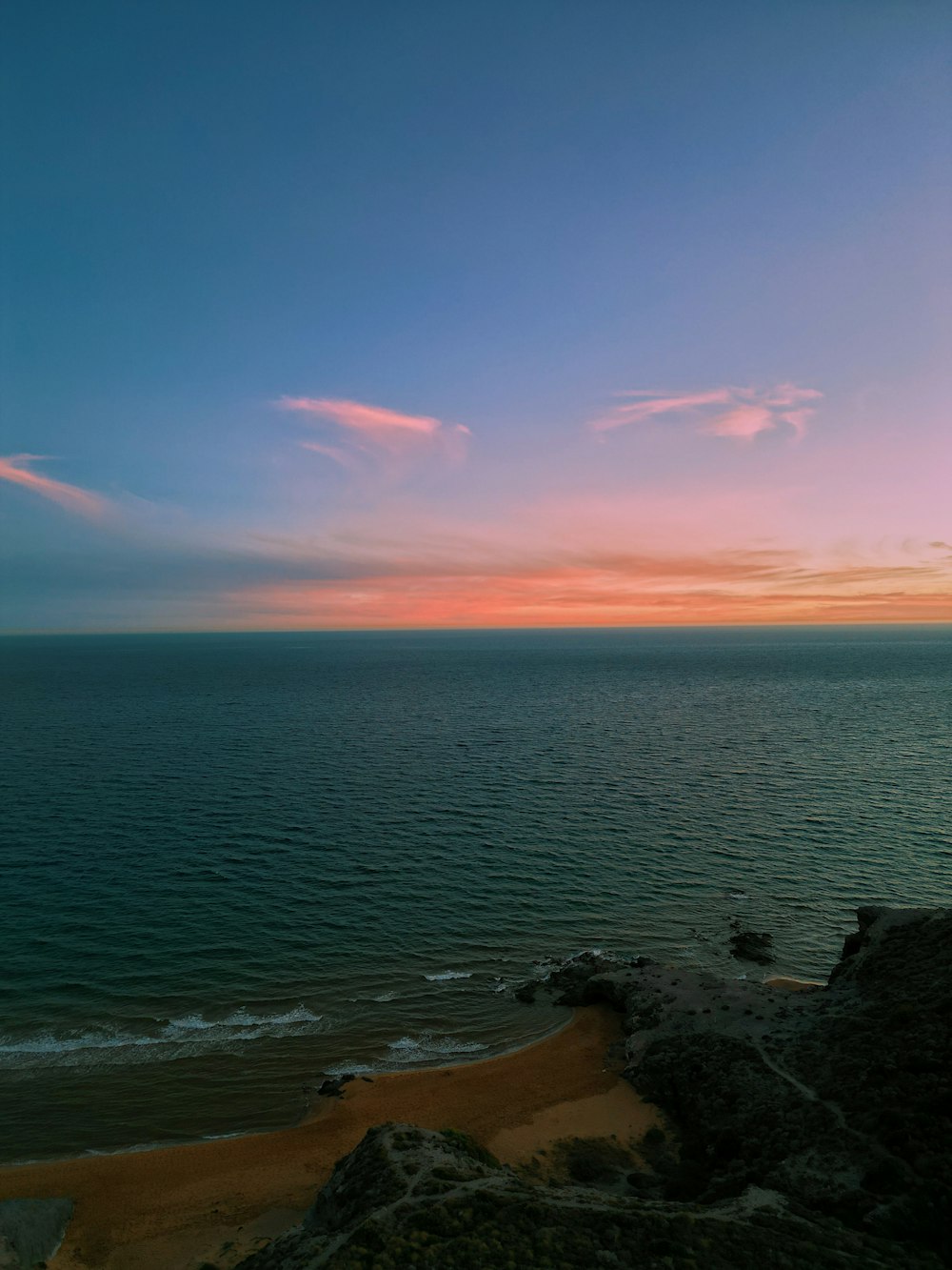 a view of the ocean at sunset from the top of a hill
