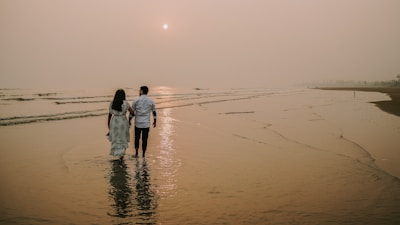 A couple walking hand in hand along a serene beach at dusk.