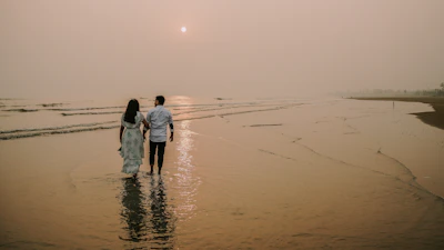Kerol and her husband walking hand in hand on a serene beach at sunset.