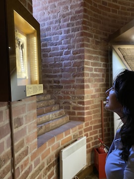 A person gazes at a lighted display case containing an artifact with detailed carvings, positioned against a brick wall. The setting appears to be a historical or museum environment with a warm atmosphere.