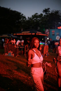 Smiling young woman wearing Kyrot earplugs at a lively outdoor music festival under a clear sky.