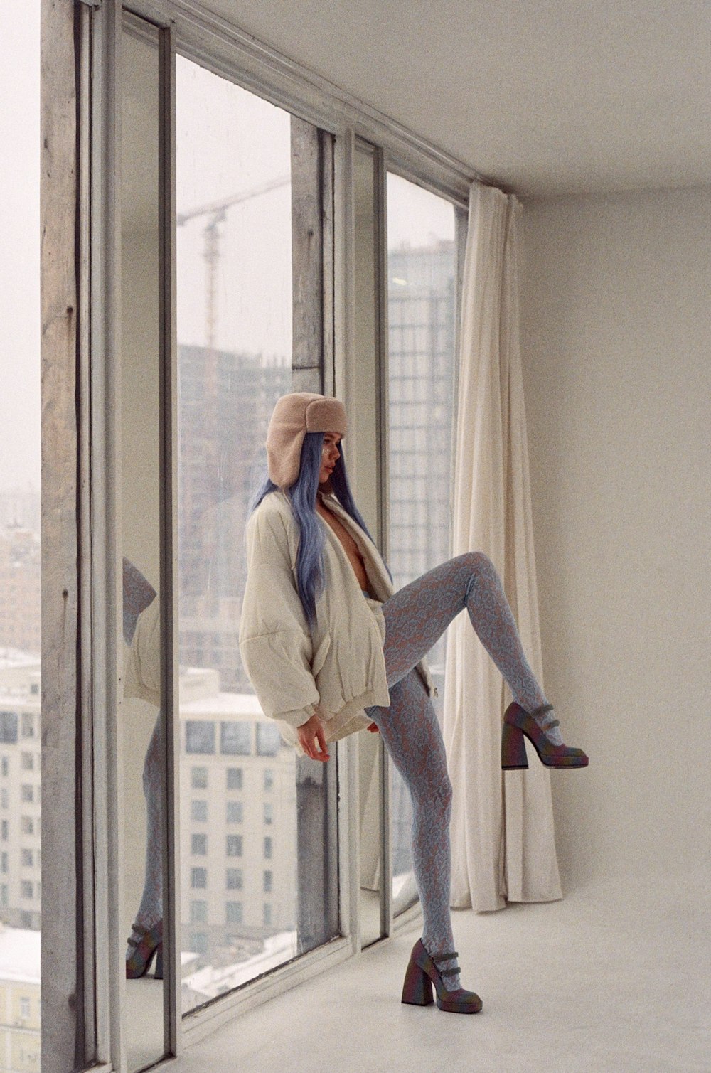 a woman with blue hair is posing in front of a window