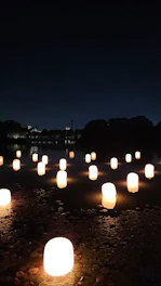 A serene night lake scene with soft purple and deep blue hues, featuring gently floating rectangular paper lanterns casting warm golden reflections on the water.