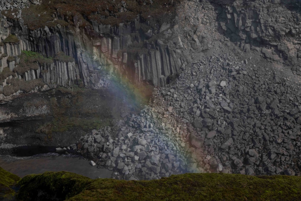 a rainbow shines in the sky over a rocky cliff