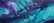A vibrant abstract painting featuring dynamic swirls and patterns with a fluid, marbled effect. The composition consists of shades of teal and purple blending harmoniously with smooth curves and circular formations, giving a sense of movement and depth.