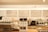 A modern coffee shop countertop with a variety of beverage options listed on the wall behind. The counter features a coffee machine, stacked paper cups, a coffee grinder with beans, and a display case with pastries. The overall aesthetic is clean and organized, with a neutral color palette.