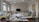 A well-lit room filled with sewing machines and various sewing materials scattered across large tables. The walls have sketches of fashion designs, and there's a chalkboard at the far end. The windows let in natural light, illuminating the workspace.