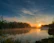 A tranquil view of the Ganga river at sunrise near Geeta Bhawan Ashram with soft saffron and light blue hues.