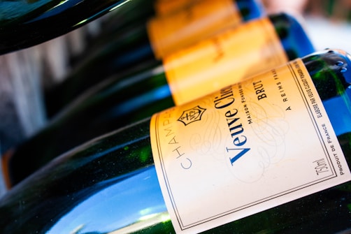 Several bottles of champagne are neatly arranged in a row, each displaying the Veuve Clicquot label prominently. The angle of the shot highlights the curve of the bottles, with a focus on the gold and blue label. The light reflects off the smooth glass surface, creating a sense of elegance and luxury.