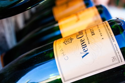 Several bottles of champagne are neatly arranged in a row, each displaying the Veuve Clicquot label prominently. The angle of the shot highlights the curve of the bottles, with a focus on the gold and blue label. The light reflects off the smooth glass surface, creating a sense of elegance and luxury.