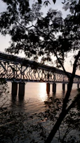A sturdy steel bridge framework rising over a flowing river, captured during golden hour.