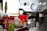 A close-up of a coffee machine with a metallic finish featuring multiple dials and buttons. In the background, there are various coffee-related items, including a bag of Peace Coffee and syrups. The scene suggests a setting for making coffee beverages.