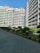 Several multi-story residential buildings with balconies, surrounded by neatly trimmed bushes and a paved walkway. The buildings have a mix of white, green, and blue colors.