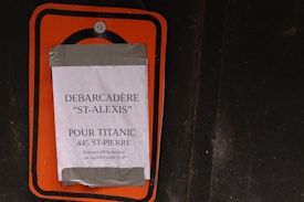 A printed sign taped to a surface using duct tape. The sign contains text in French with instructions related to 'St-Alexis' and 'Titanic,' mentioning an address '445 St-Pierre.'