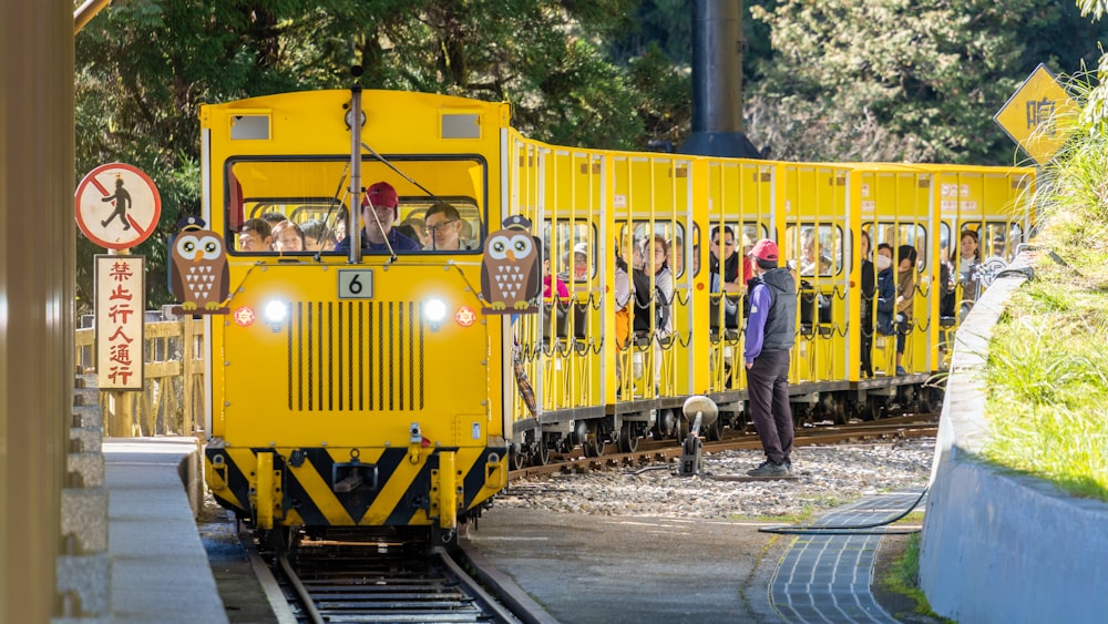 Un tren amarillo que viaja por las vías del tren junto a un bosque