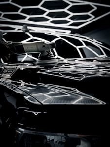 Technician carefully polishing a sleek car exterior with dual-action polisher under natural daylight.