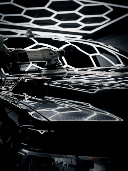 Technician carefully polishing a sleek car exterior with dual-action polisher under natural daylight.