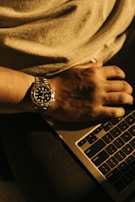 A wristwatch worn by a person typing on a laptop in a cozy café setting.