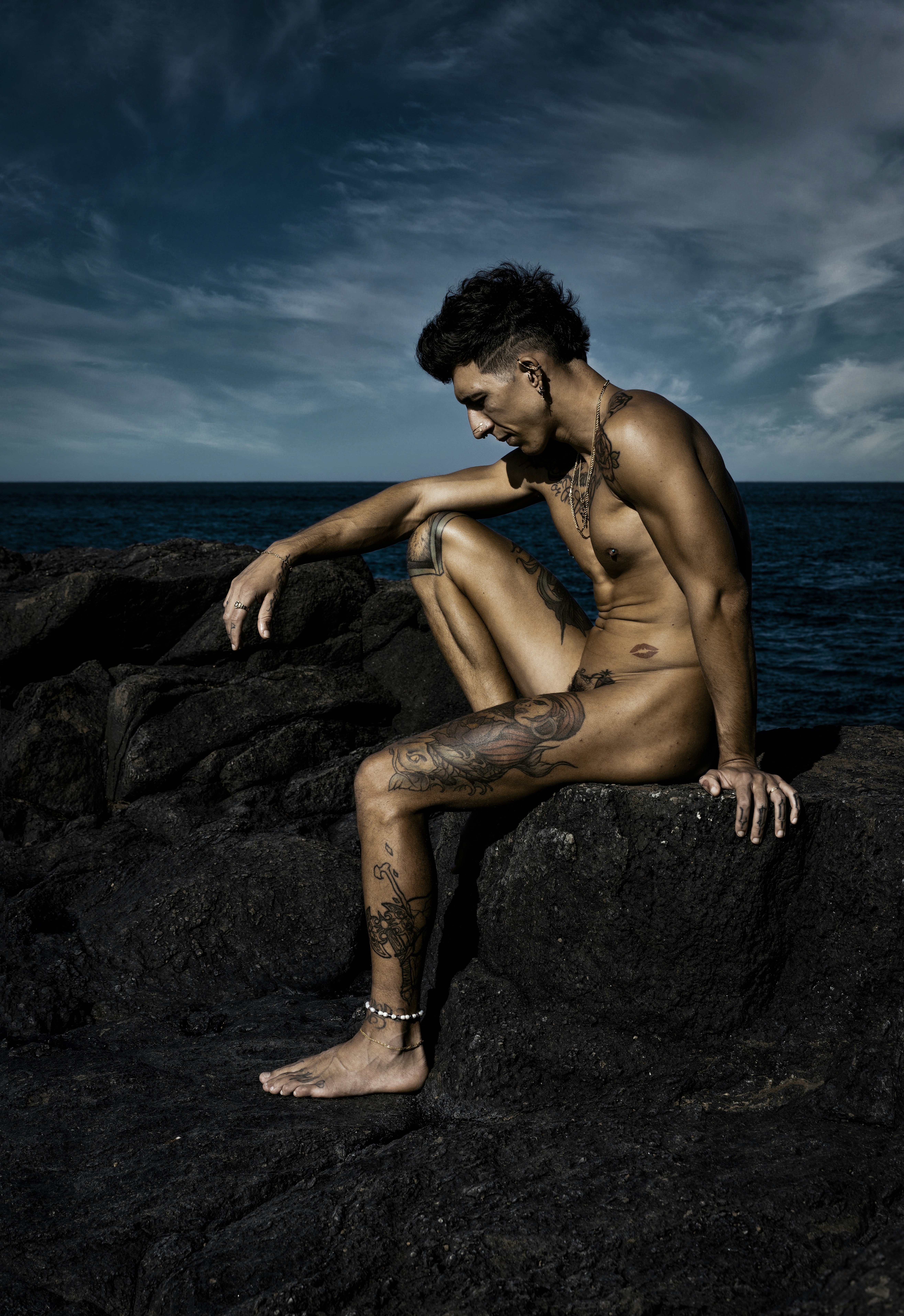Homme nu prenant le soleil assis sur un rocher en bord de plage.