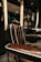 A luxurious barber chair with dark brown leather upholstery featuring white piping, set in an upscale barbershop. The chair is positioned next to shelves containing various bottles, likely grooming products or refreshments. The shop has a modern and elegant interior design, with dark colors and subtle lighting contributing to an overall sophisticated atmosphere.