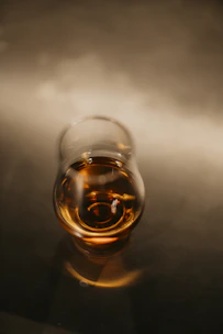 A glass of louvel brandy with amber liquid catching the light, set against a backdrop of toasted French oak barrels.