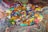 A vibrant artist's palette filled with a variety of acrylic colors is displayed against a swirling, colorful background. The palette itself is covered in thick, textured blobs and strokes of paint in shades of blue, green, orange, red, and yellow, among others. The background features a mesmerizing marbled pattern in a similar color scheme, enhancing the chaotic yet artistic feel.