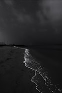 A dark, nighttime beach scene with waves glowing with bioluminescence along the shoreline under a starry sky.