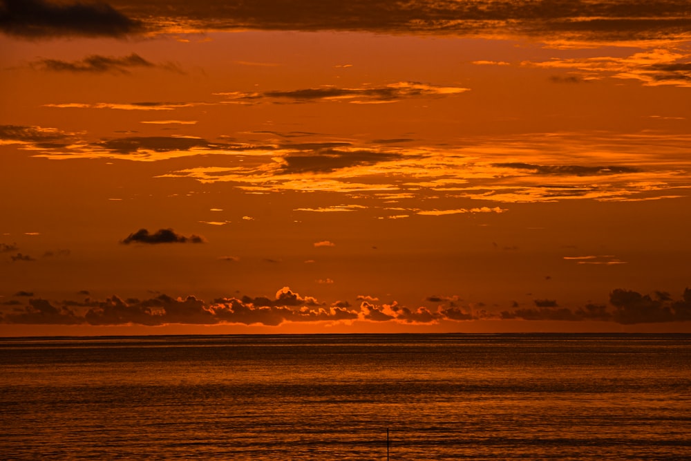 the sun is setting over the ocean with a sailboat in the foreground