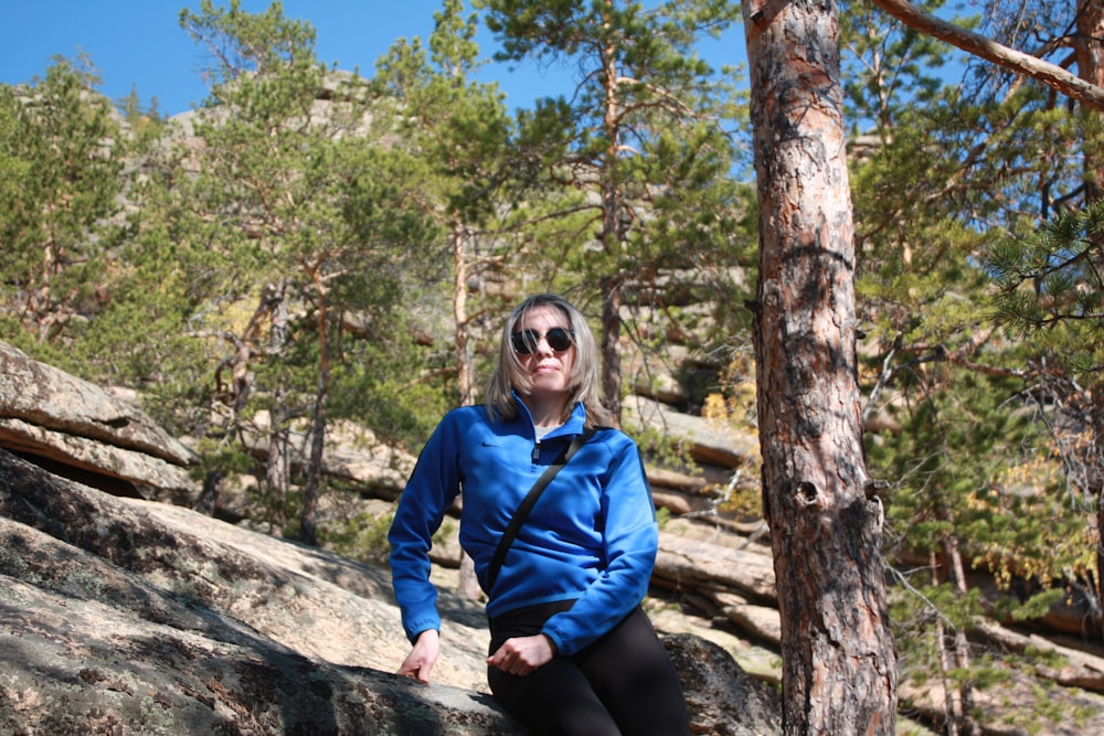 a woman sitting on a rock in the woods