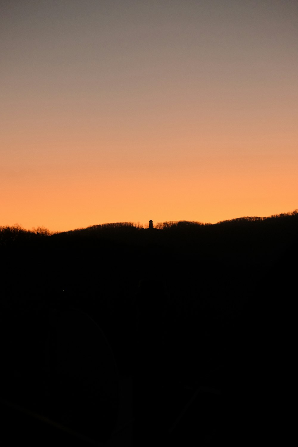 a silhouette of a person standing on a hill at sunset